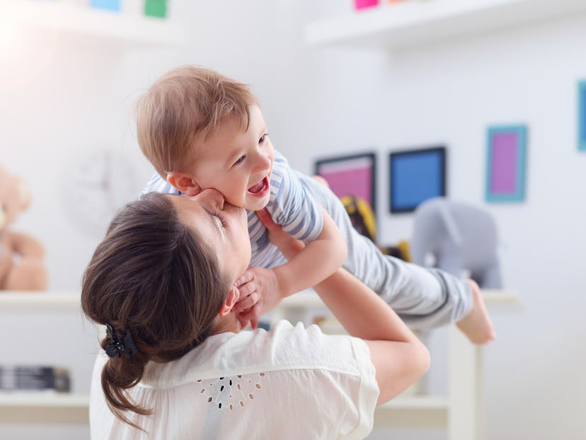 Mom holding up her toddler and kissing him on the cheek while he laughs