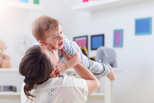 Mom holding up her toddler and kissing him on the cheek while he laughs