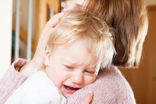 A closeup of a kid crying in his mother's arms due to the pain caused by his ear infection