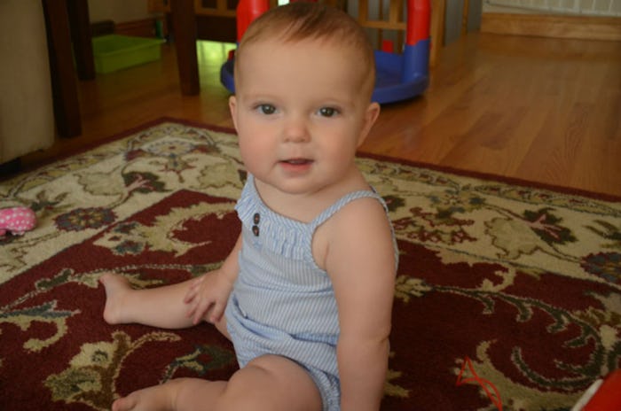 A baby in a light blue romper sitting on a carpet on the floor