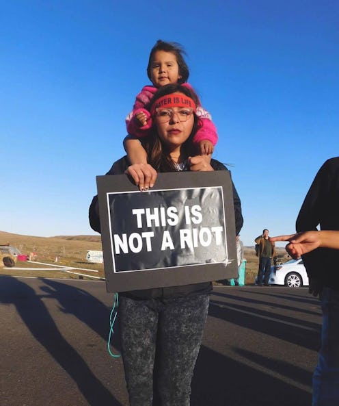 Eryn Wise, Jicarilla Apache carrying her daughter on her shoulders while carrying a protest sign rea...