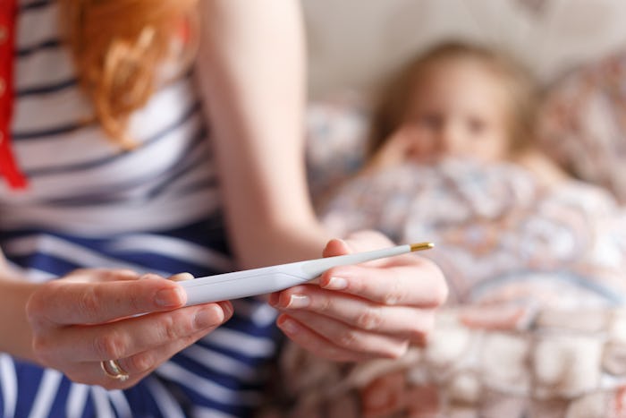 A child lying in bed while her mother sits next to her and looks at the thermometer