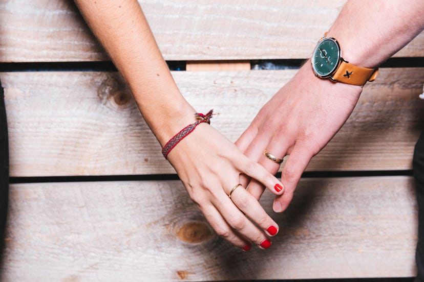 A couple holding hands in front of a wood wall, both experiencing shaky hands