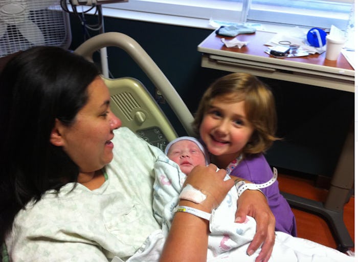 Candace Ganger lying in a hospital bed after giving birth, holding her newborn baby while her daught...