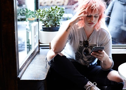 A woman with pink hair sitting down and looking at her phone recovering from dizziness