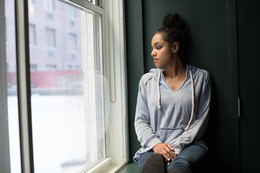 A woman experiencing depression and mood swings sitting on a window sill and looking outside