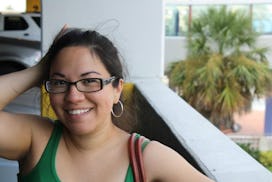 A woman in a green tank top and glasses smiling even though she feels lonely during pregnancy