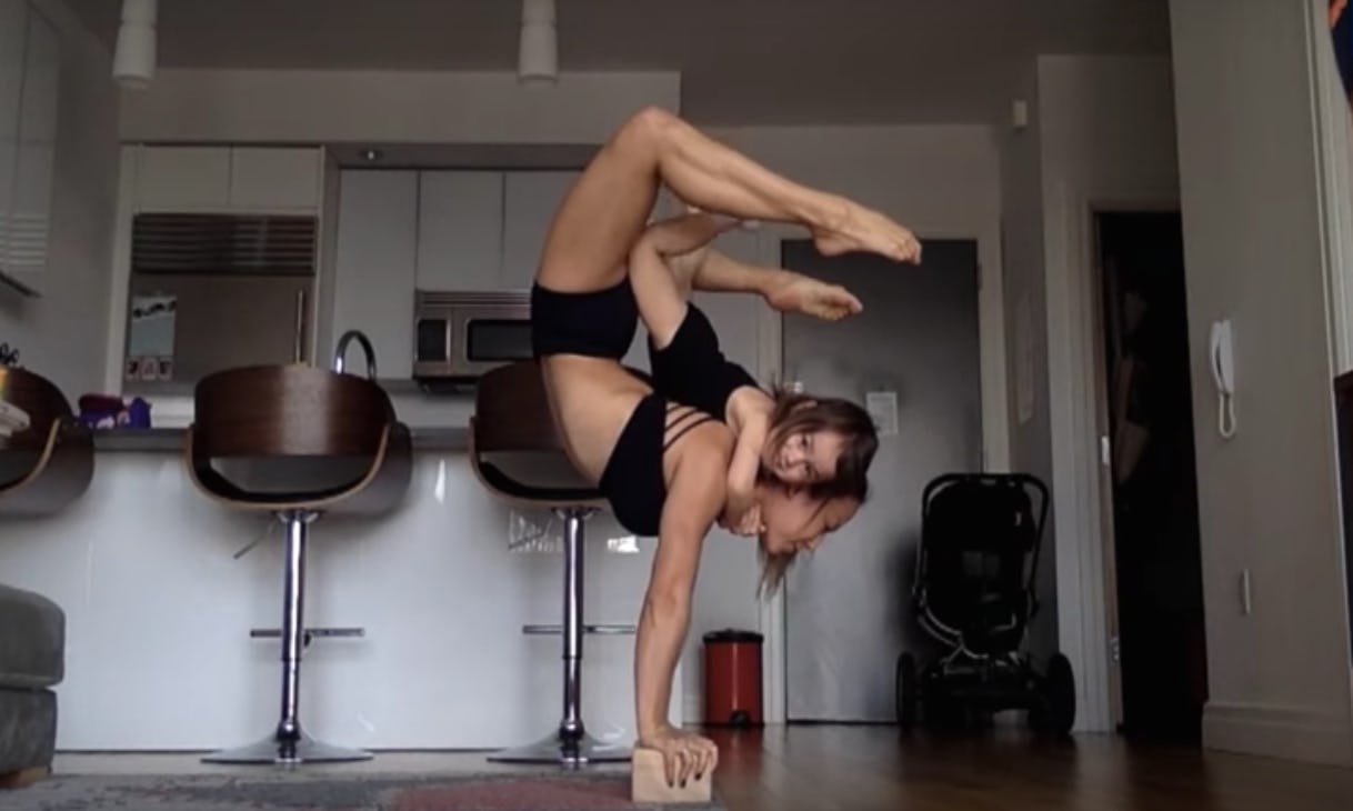 A mom doing a yoga handstand while carrying her daughter on her back