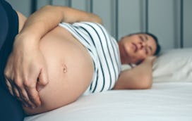 A pregnant woman holding her stomach while lying in bed with insomnia
