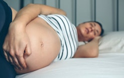A pregnant woman holding her stomach while lying in bed with insomnia