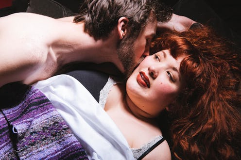 A red haired woman lying in bed being kissed on the cheek by a naked man