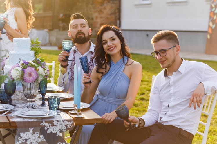A happy couple holds up their glasses to cheers to the happy couple at a wedding outdoors.