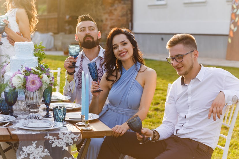 A happy couple holds up their glasses to cheers to the happy couple at a wedding outdoors. 