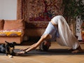 A girl doing a yoga pose to stop her headache with her dog laying in front of her