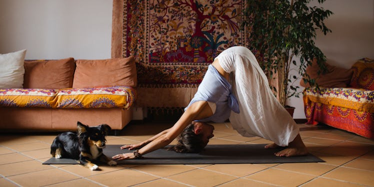 A girl doing a yoga pose to stop her headache with her dog laying in front of her