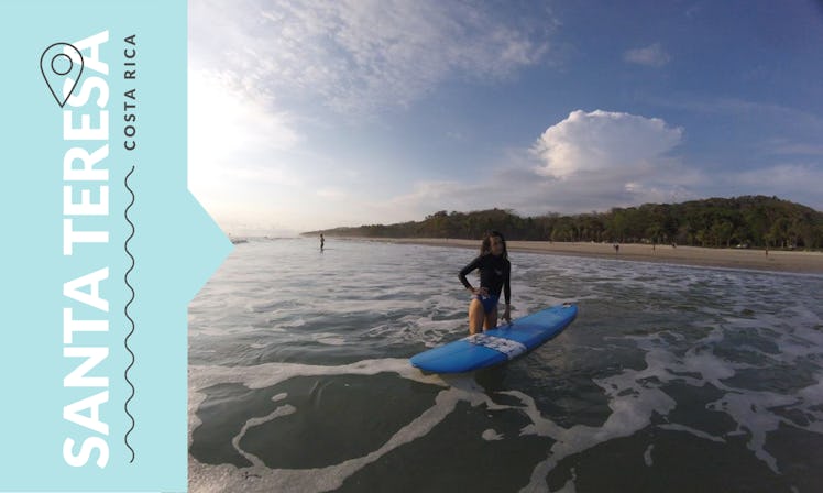 A young woman standing in the sea leaning on a surfboard in Santa Teresa, Costa Rica.