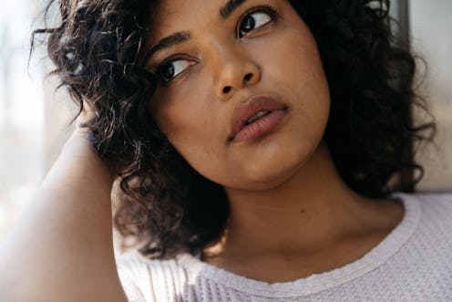 A young curly-haired, religious woman sitting next to a window and thinking about getting an abortio...