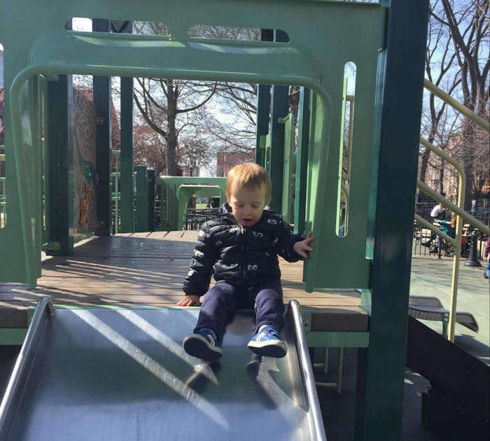 A little boy riding down a park slide