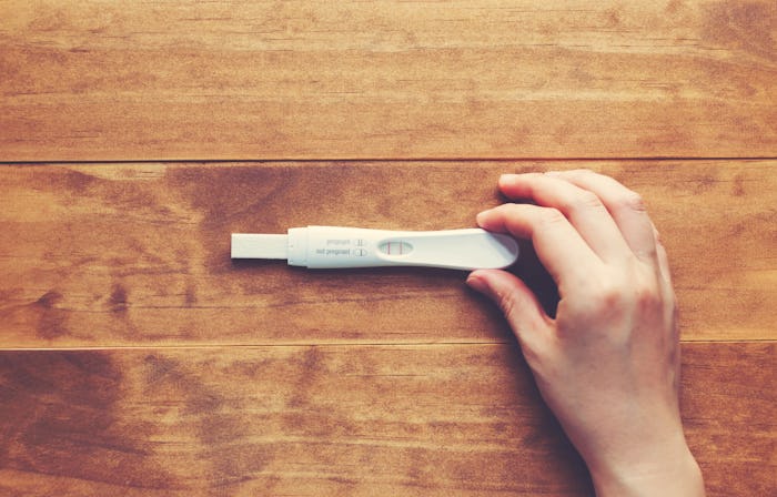A woman holding a pregnancy test on a wooden surface during the silent months of pregnancy