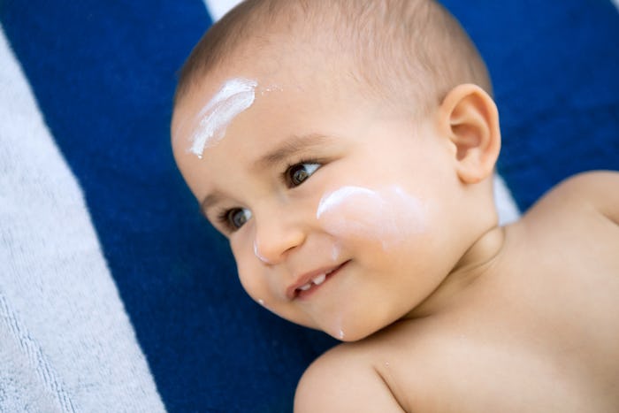 A baby lying on its back on a towel with sunscreen on its forehead and cheeks