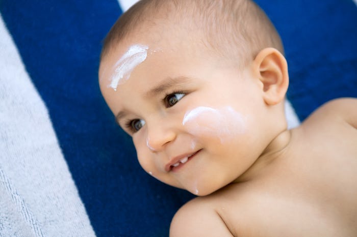 A baby lying on its back on a towel with sunscreen on its forehead and cheeks