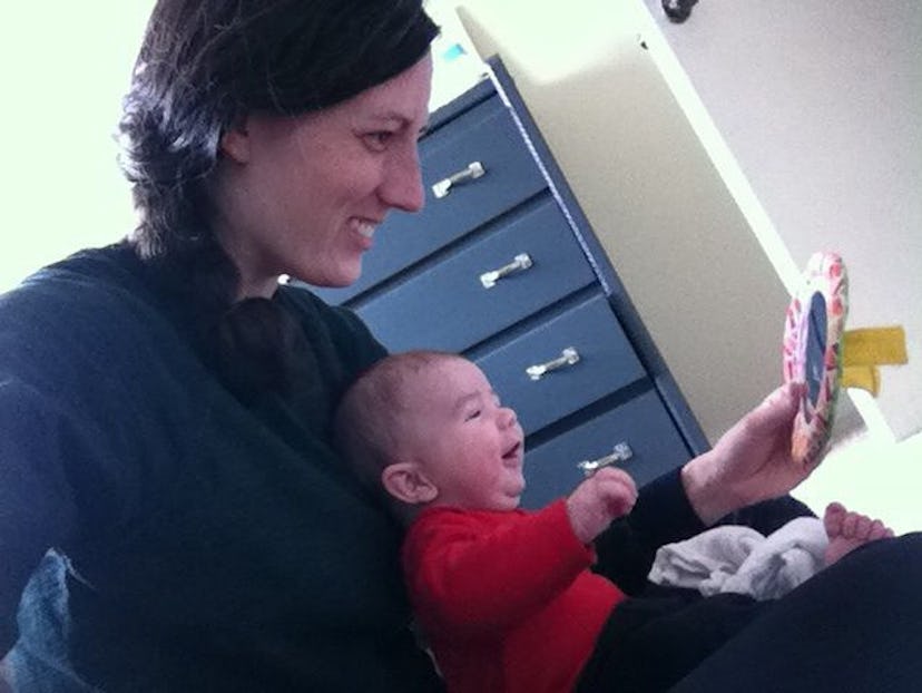 A woman is showing the baby its face in the mirror with the baby smiling.