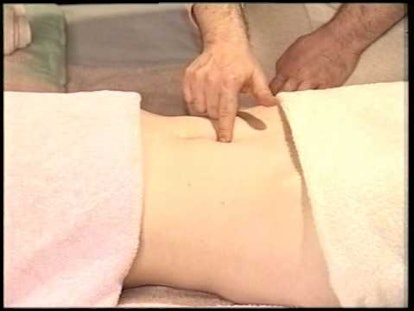 A woman lying on her back with period cramps and a finger pointing two finger-widths below her navel