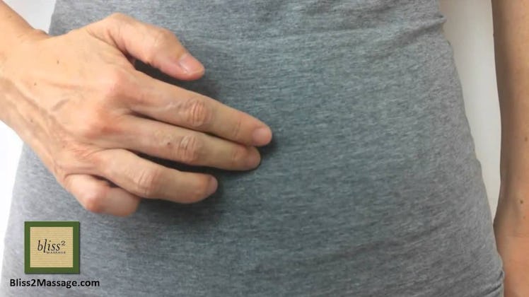 A woman in a grey shirt holding two fingers over her stomach