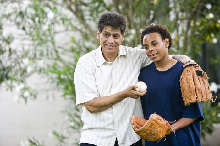 A dad hugging his teen son while holding a baseball, both wearing baseball gloves.