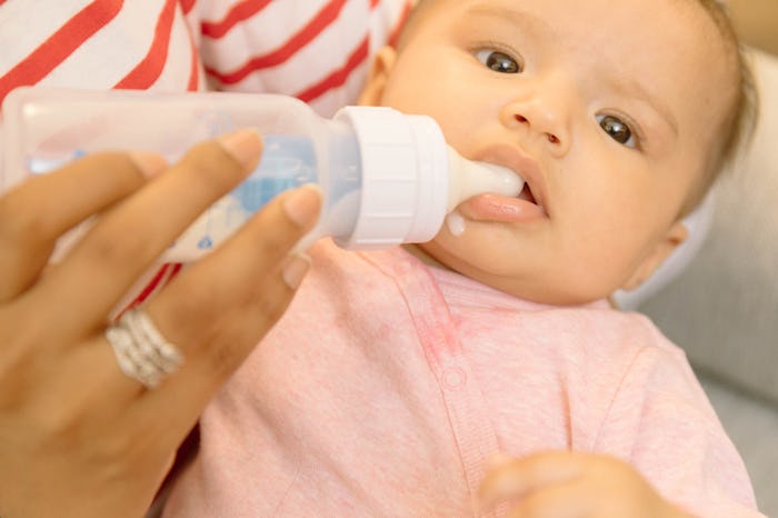 A baby drinking formula out of a bottle with the help of its mother