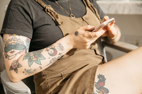 A woman with tattoos, a black top and brown dress using her phone to schedule an abortion