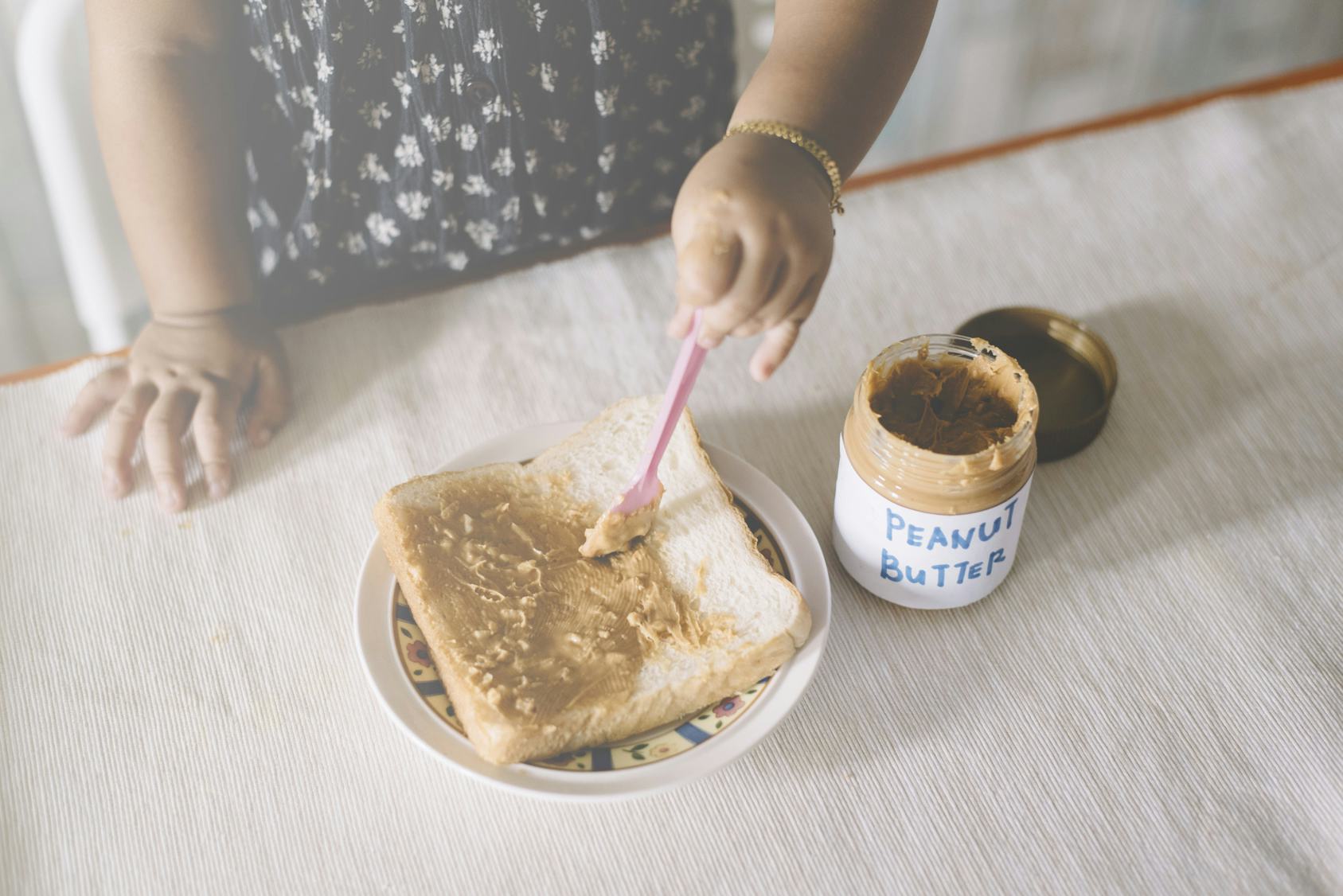 A child spreading peanut butter on a piece of white bread.