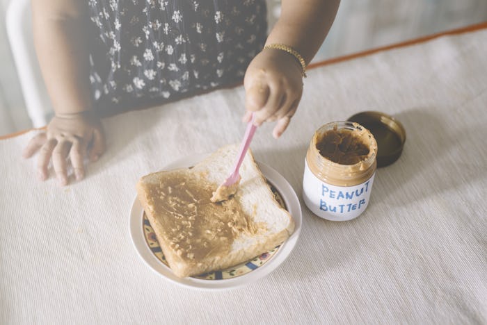A child spreading peanut butter on a piece of white bread.