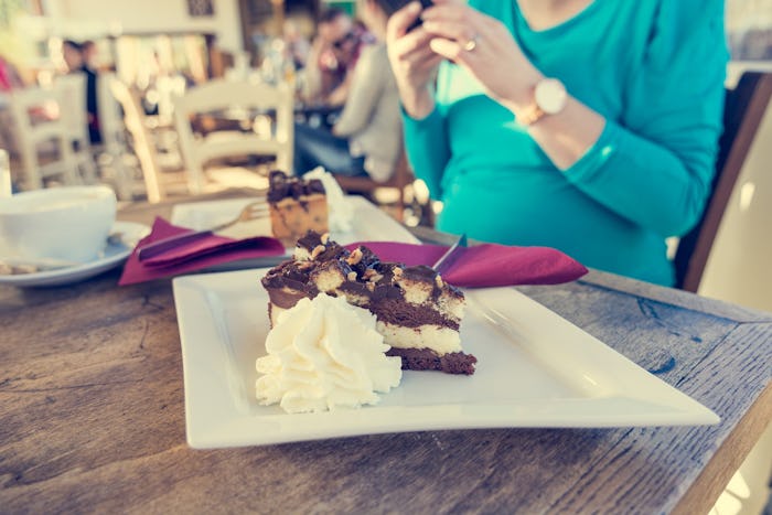 A pregnant woman craving chocolate eating a cake in a restaurant.