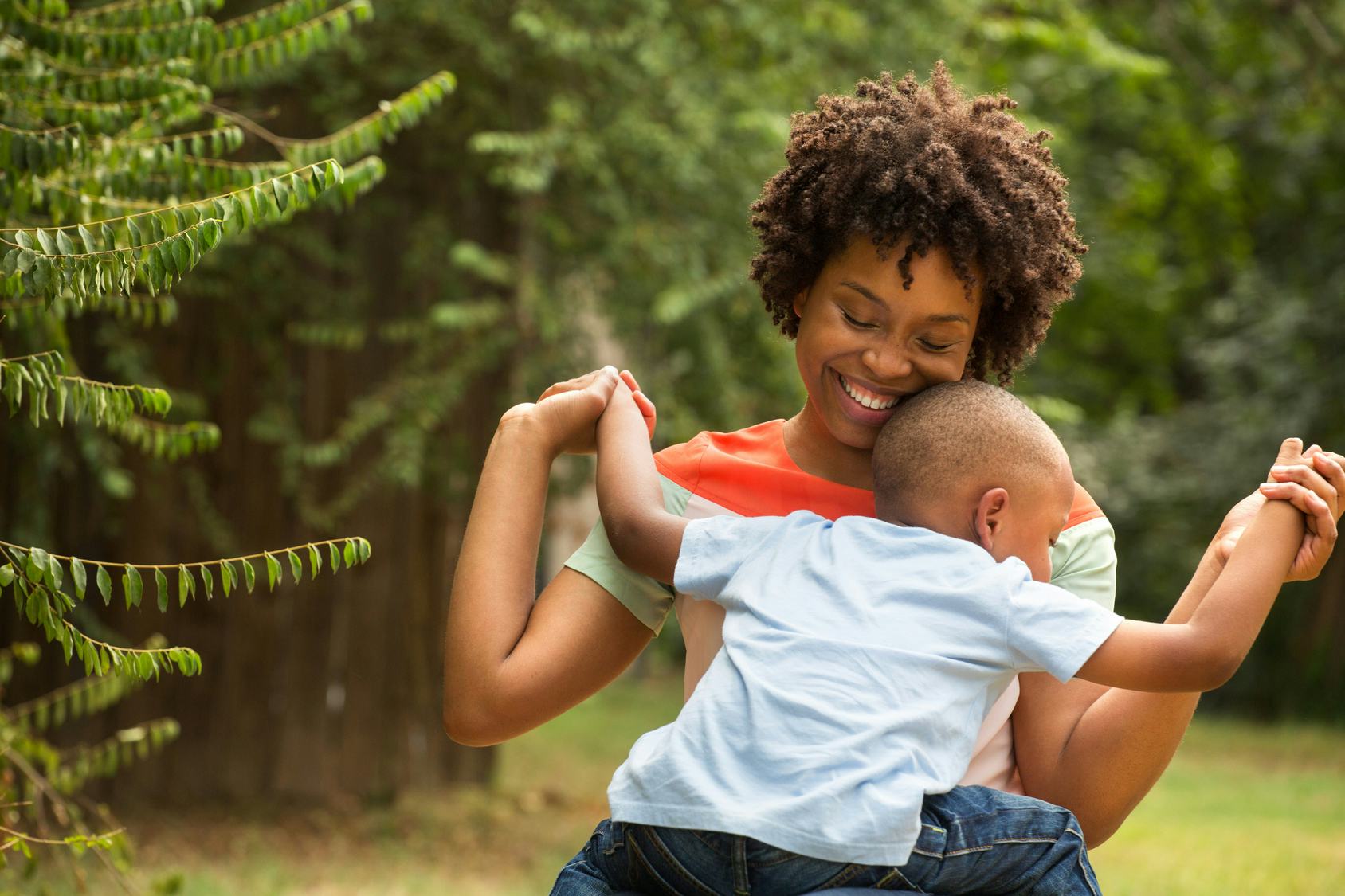 A curly-haired mother smiling and holding her kid while she's playing with him