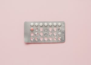 A pack of birth control pills on a pale pink surface