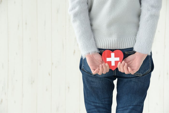A woman struggling with pregnancy hemorrhoids holding a red paper heart with a white cross on her ba...