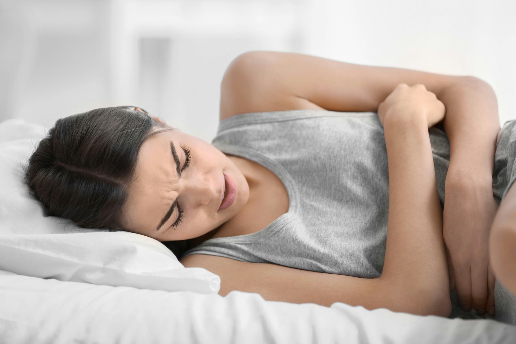 A woman in bed, holding on to her stomach in pain because of endometriosis 