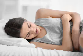 A woman in bed, holding on to her stomach in pain because of endometriosis