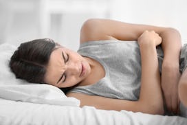 A woman in bed, holding on to her stomach in pain because of endometriosis 