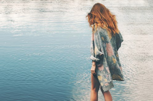 A red-haired girl in a floral shirt walking towards the sea.