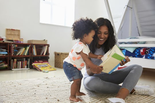 A millennial parent and their child sitting in the bedroom reading a book about human body parts