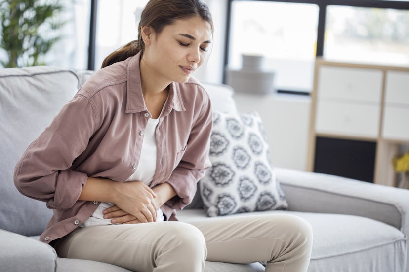 A woman sitting on her couch dealing with gas by holding her hands to her stomach