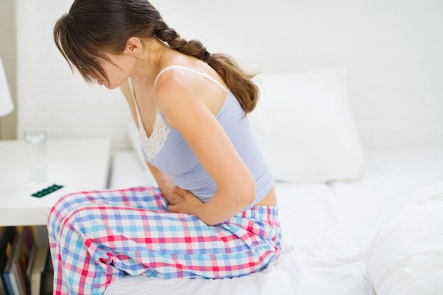 A woman feeling bloated sitting on her bed in pajamas and holding her stomach