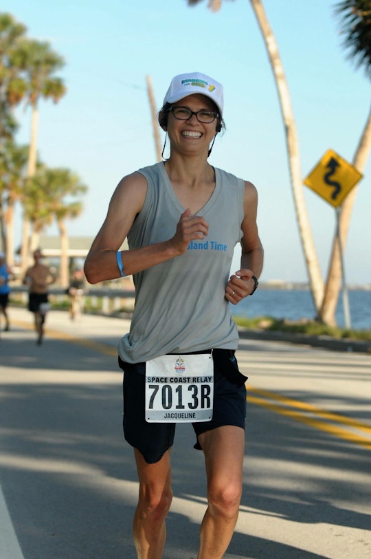 A man in a grey tank top and a cap running a marathon while smiling at the camera