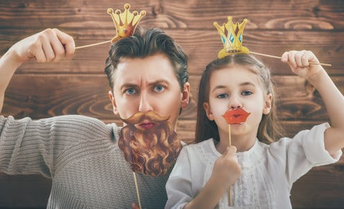 A father and daughter posing for a photo with paper decorations on stick in forms of crown, lips and...