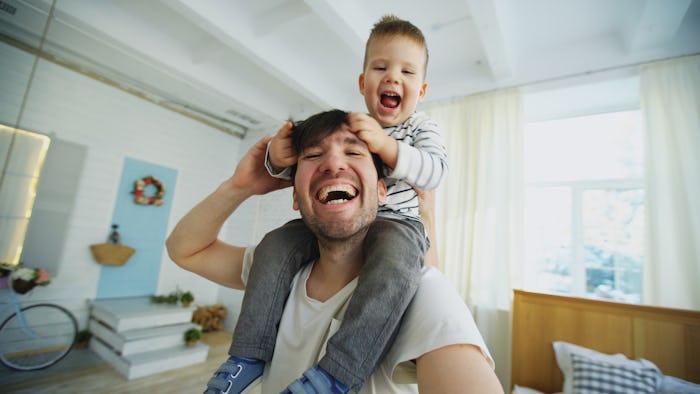 A dad laughing while carring his son on his shoulders through the house taking a selfie