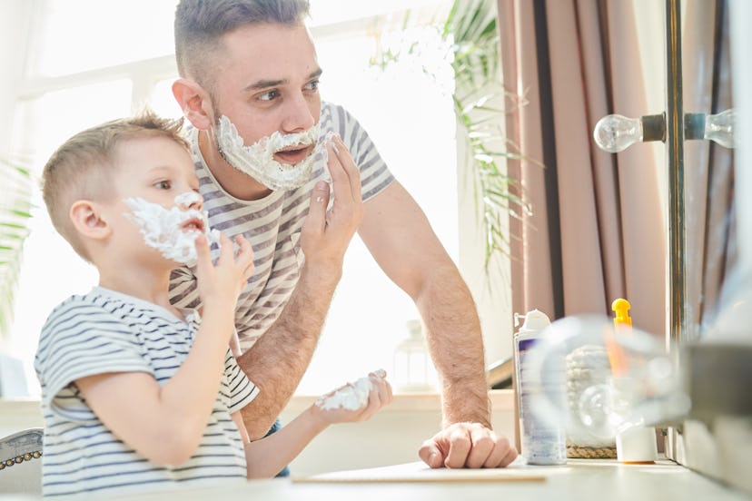 Father and his small son in front of the bathroom mirror, covered with shaving foam