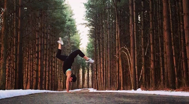 A woman standing on her hands in the middle of a forest