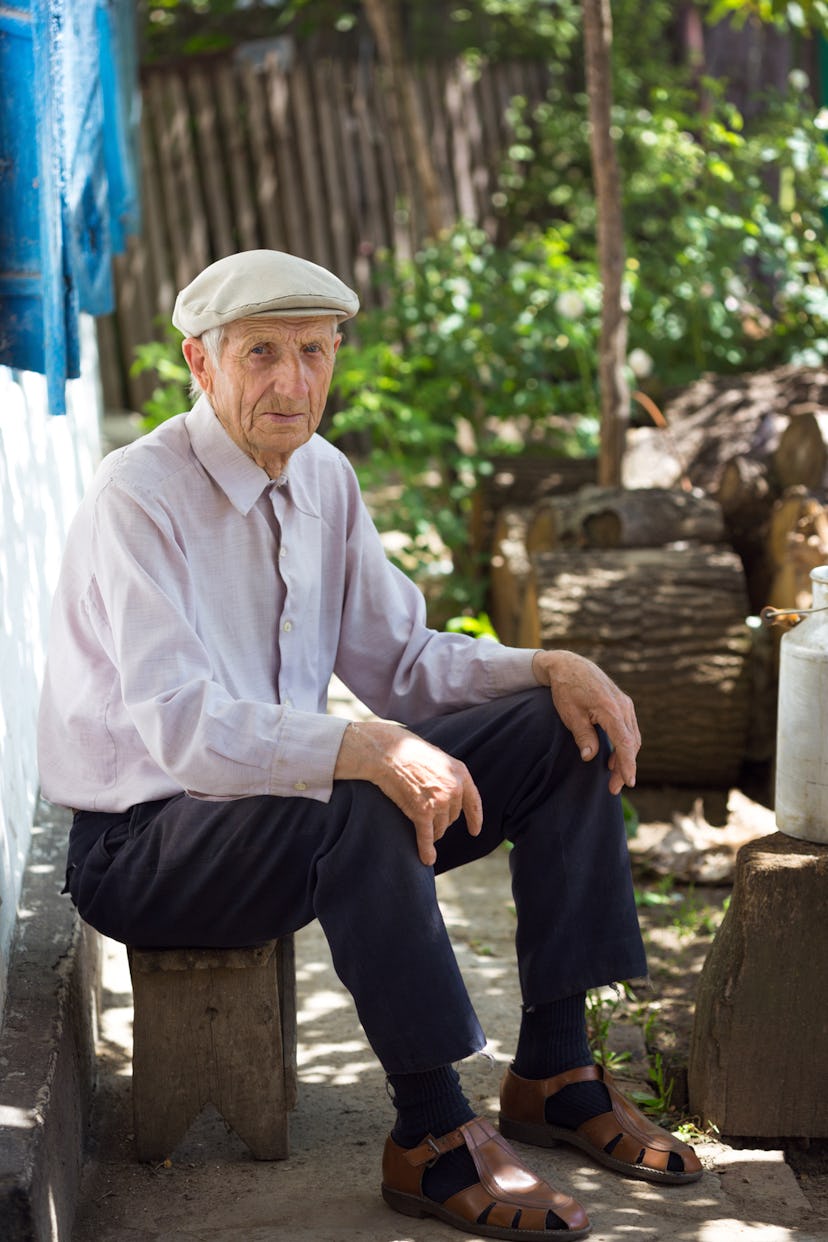 Old man with a gray hat and shirt sitting on a small chair in the countryside